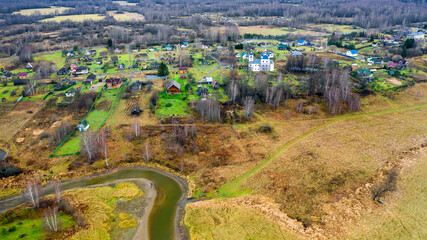 Aerial view of the village on a high hill above the river at sunrise in autumn. Aerial view. Residential buildings and a church, river bends, meadows, orange grass, trees at dawn.