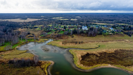 Obraz premium Aerial view of the village on a high hill above the river at sunrise in autumn. Aerial view. Residential buildings and a church, river bends, meadows, orange grass, trees at dawn. 