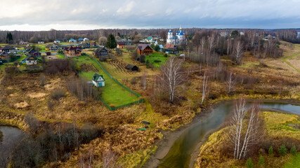Fototapeta na wymiar Aerial view of the village on a high hill above the river at sunrise in autumn. Aerial view. Residential buildings and a church, river bends, meadows, orange grass, trees at dawn.