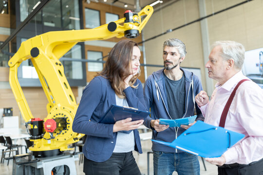 Engineers in factory having meeting in front of industrial robot