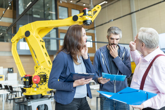 Engineers in factory having meeting in front of industrial robot