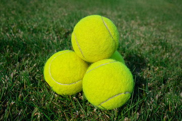 A group of tennis balls stacked in a pyramid on grass. Generic furry fuzzy yellow tennis balls on grass  