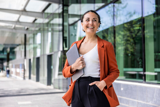 Smiling businesswoman holding laptop standing with hand in pocket