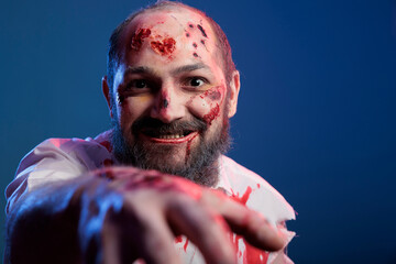 Creepy halloween zombie approaching camera in studio, looking spooky and dangerous with bloody...