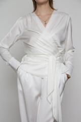 Serie of studio photos of young female model wearing all white classic outfit, silk satin wrap blouse and wide legged trousers.