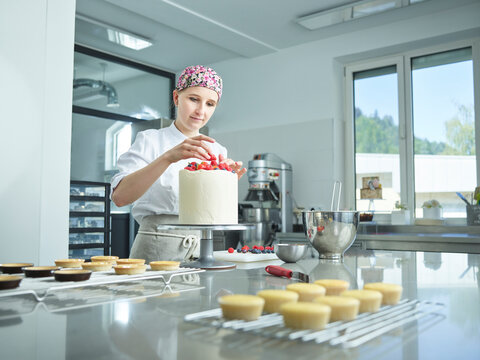 Young confectioner decorating cake with strawberries in kitchen