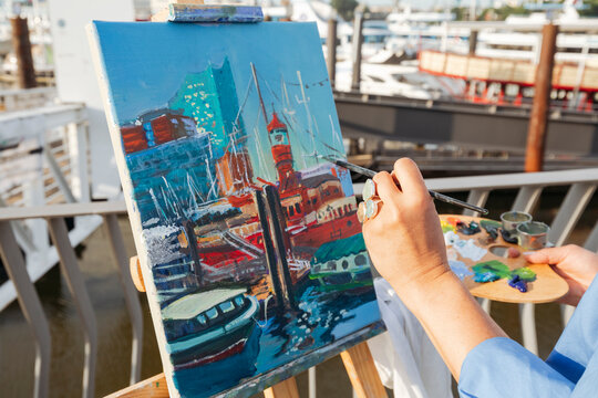 Hand of artist painting on easel at harbor
