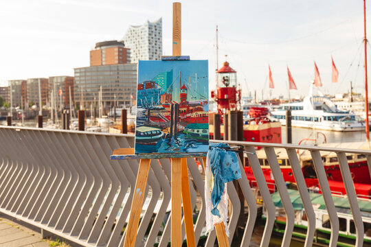 Painting on easel in front of boats at harbor