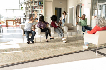 Smiling businessmen and businesswomen greeting colleague walking in office