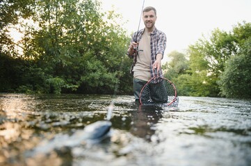 Fisherman catches a trout on the river in summer