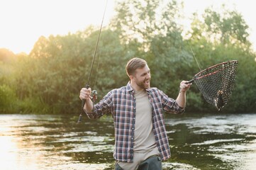 Man with fishing rod, fisherman men in river water outdoor. Catching trout fish in net. Summer...