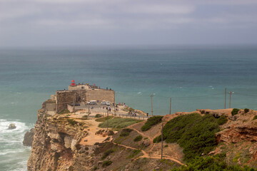 Fototapeta na wymiar Fort at seaside of Portugal, Nazare. Lighthouse on the rocky cliff