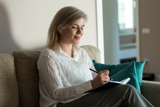 Smiling Mature Woman Writing In Diary At Home