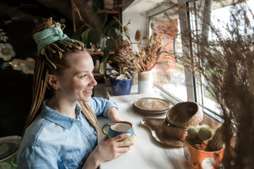 Happy potter with ceramic cup looking through window at workshop
