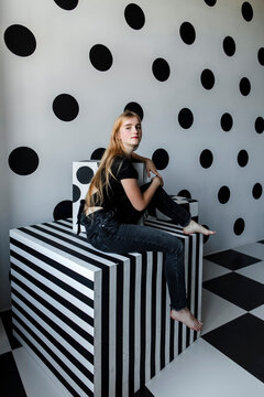 Girl sitting on cube shape box by wall
