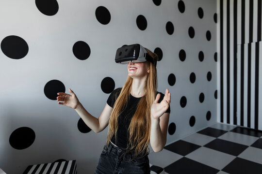 Happy girl enjoying wearing virtual reality headset by dotted wall - Powered by Adobe