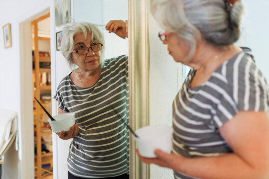 Senior woman examining white hair looking in mirror at home