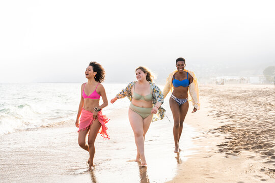 Multiracial friends in swimwear walking near seashore at beach