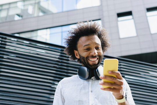 Happy Man With Headphones Using Smart Phone In Front Of Building