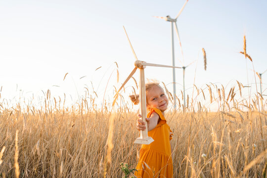 Playful Girl Holding Wind Turbine Model In Wheat Field