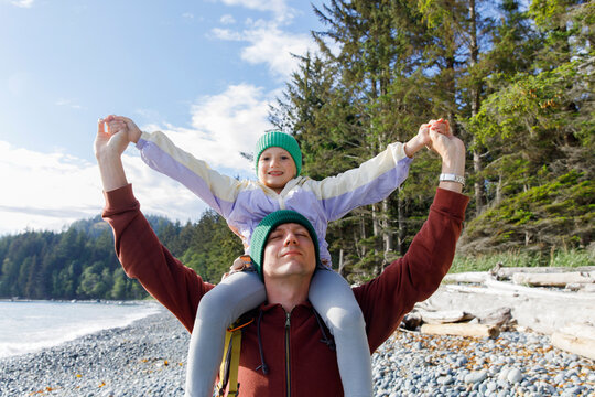 Father with eyes closed carrying daughter on shoulder at beach