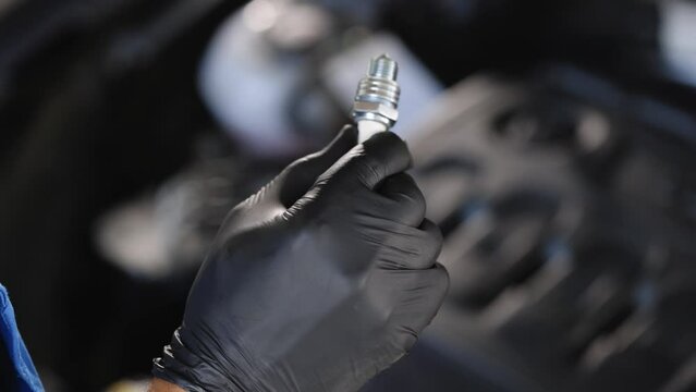 Male auto mechanic changes spark plugs in a car engine. Close up of worker hands changes spark plugs in car engine in auto service. An auto mechanic replaces the spark plugs in the car