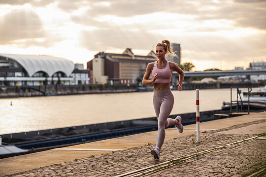 Blond woman jogging in front of river at sunset