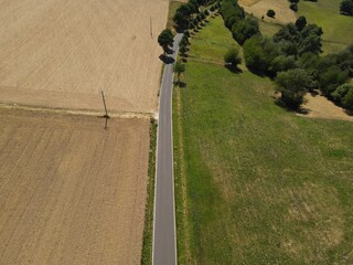 Aerial view of a rural asphalt road between agriculture fields and grassfields on a sunny day in summer 
