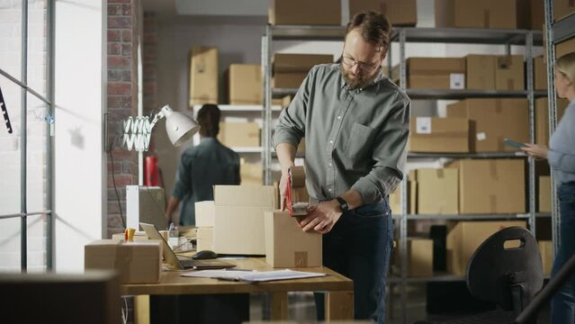 Stylish Storeroom Worker Preparing a Small Parcel for Postage. Inventory Manager Taping a Cardboard Box Before Shipping It to Customer. Small Business Owner Working in Warehouse Facility.