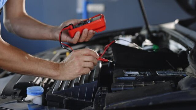 Professional car mechanic check battery voltage with electric multimeter. Automobile diagnosis. Car mechanic repairer looks for engine failure on diagnostics equipment in vehicle service workshop