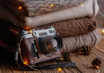Vintage film camera and stack of knitted items on wooden background