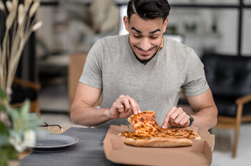 Joyful man looking at pizza taking slice