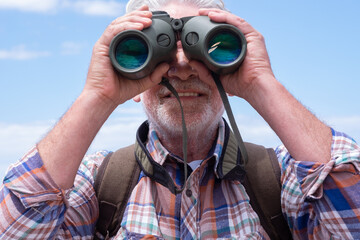 Close up on active senior man  in outdoors excursion using binoculars looking at camera, elderly...