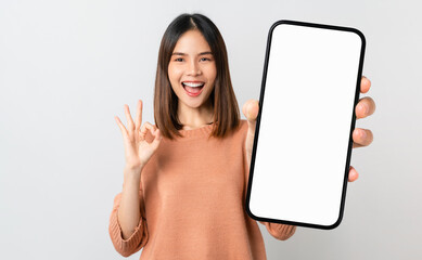 Beautiful Asian woman holding smartphone mockup of blank screen and shows ok sign on grey background - Powered by Adobe