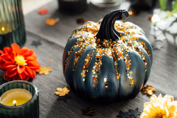 Close up gray pumpkin with sequins, burning candles and fresh dahlia flowers on the textile napkin....