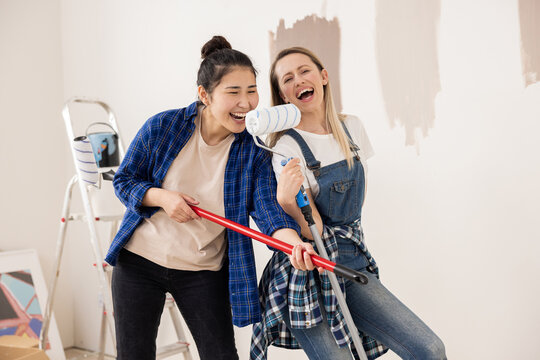 Blonde girl and women with black hair imagined that they were pop stars on stage. In fact friends are renovating apartment and sing not into microphones but into paint rollers.