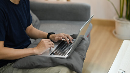 Cropped view of man sitting on couch and working online or surfing internet with laptop