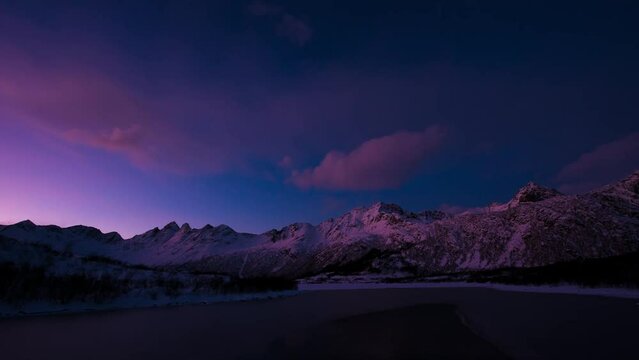 Video time-lapse of movement of pink and purple clouds in the blue sky from dusk to the night, over Lofoten islands in Norway, the clouds run in the sky from left to right, above a small cove fiord