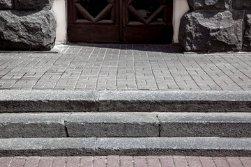 granite steps on a pedestrian pavement made of stone tiles near a building with entrance a wooden...