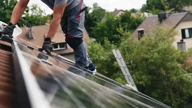 Man carefully lands solar panel on top of rooftop into place, side view