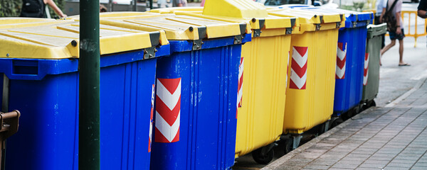 Blue and yellow trash containers standing on sidewalk at city street outside