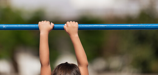 Fototapeta premium Child playing sports on the playground outdoors, child on the crossbar