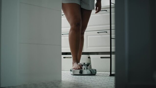 Legs of unrecognizable African-American woman stepping on the bathroom scale. Shot with RED helium camera in 8K. 