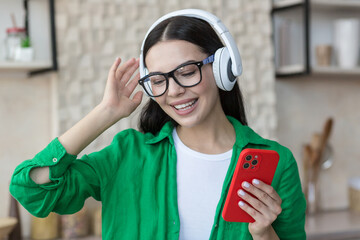 Close-up photo. Happy young beautiful female in green clothes and glasses listening to music in...