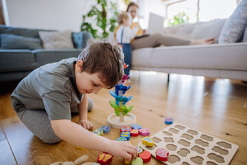 Little boy playing with montessori wooden toys in living room,mother and sister in backgroud.