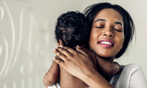 Portrait of enjoy happy love family african american mother playing with adorable little african american baby.Mom kiss with cute son moments good time in a white bedroom.Love of black family