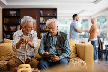 Senior male friends surfing the net on touchpad while relaxing in nursing home.