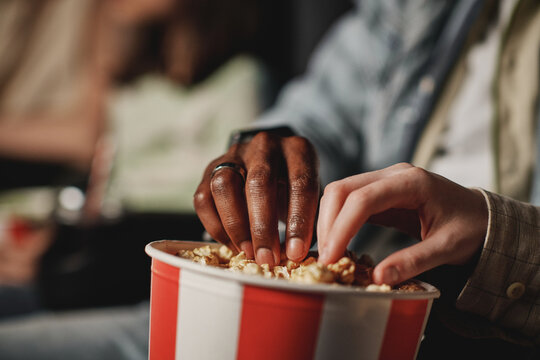 Selective focus of unrecognizable ethnically diverse man and woman in love eating popcorn while watching movie at cinema