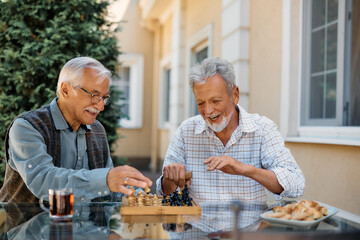 Happy senior men having fun while playing chess on patio.