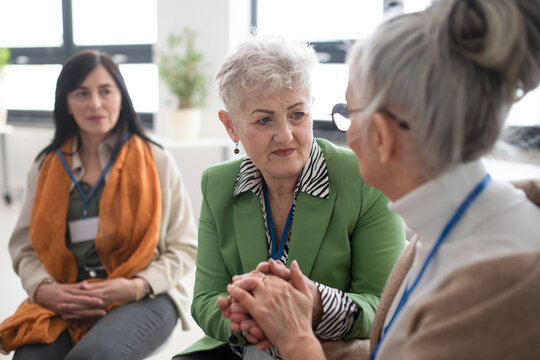 Group of senior people sitting in circle during therapy session, consoling depressed woman. - Powered by Adobe